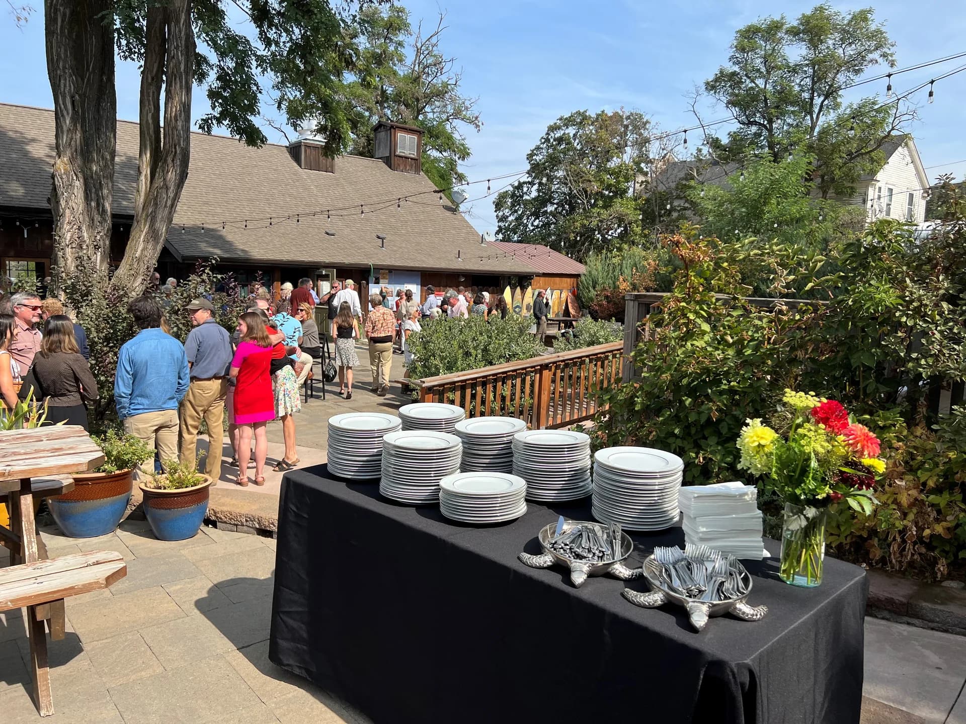 Elegant outdoor wedding event setup with string lights, flower arrangements, and plate stacks by Taste of Pearl