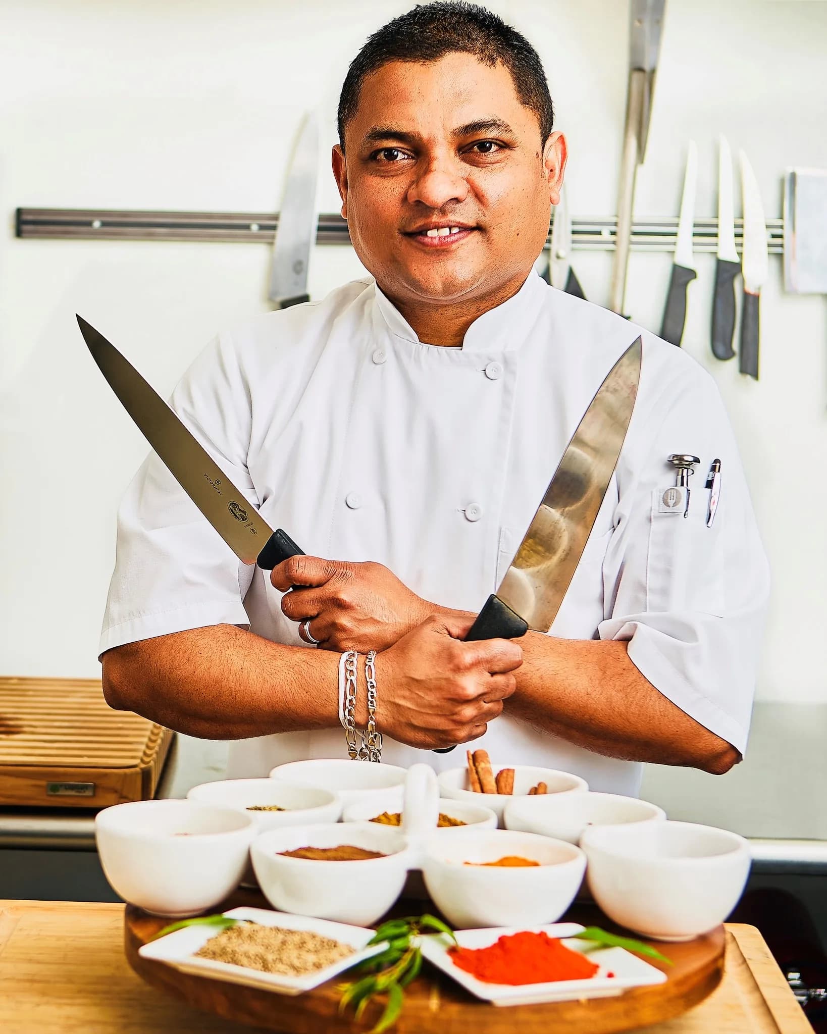 Chef Kal with crossed knives and bowls of spices — an editorial portrait